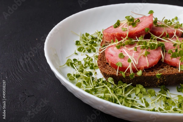 Obraz Sandwich with bread and sausage slices, decorated with homegrown fresh harvested broccoli cabbage microgreen sprouts on white plate. Close up