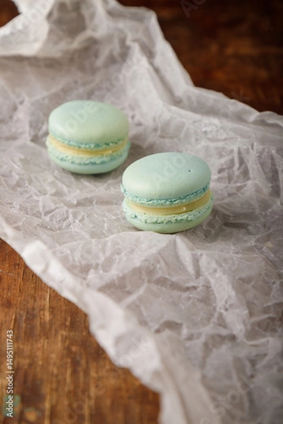 Obraz Tender green macaroons with pistachio flavor filling on paper, wooden background. Copy space.