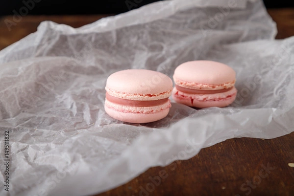 Obraz Tender pink macaroons on paper, wooden background. Forest berries, strawberry or raspberry flavor