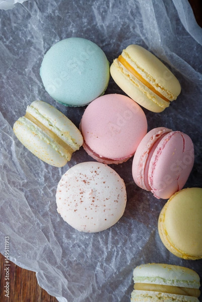 Obraz Tender multicolored macaroons with different flavors on paper, wooden rustic background. Top view, closeup shot