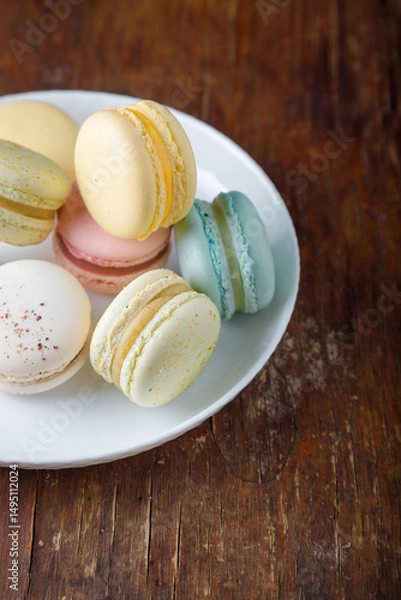 Obraz Tender multicolored macaroons with different tastes on white plate, wooden old table background, top view closeup shot