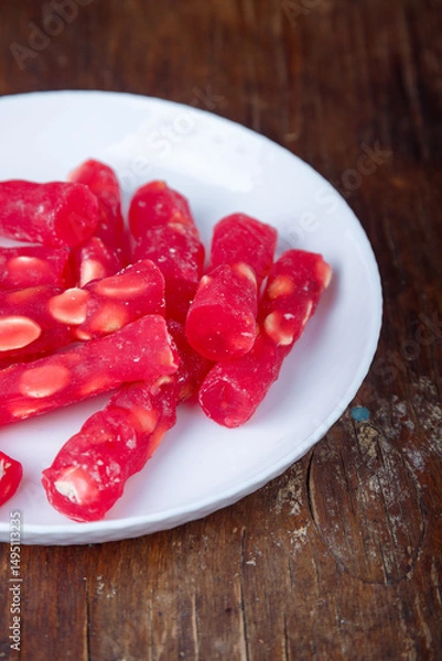 Obraz Turkish delight, red locum sticks with hazelnut on white plate, wooden background. Eastern sweets, oriental food. Traditional tasty dessert. Copy space. Top view