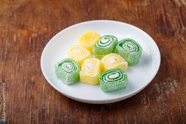 Obraz Turkish delight, yellow and green locum roll with coconut flakes on white plate, wooden background. Eastern sweets, oriental food. Traditional tasty dessert. Copy space. Top view