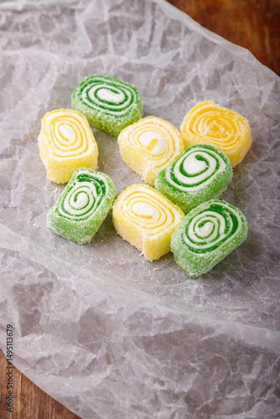 Obraz Turkish delight, yellow and green locum roll with coconut flakes on white paper, wooden background. Eastern sweets, oriental food. Traditional tasty dessert. Copy space. Top view