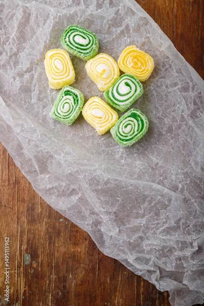 Obraz Turkish delight, yellow and green locum roll with coconut flakes on white paper, wooden background. Eastern sweets, oriental food. Traditional tasty dessert. Copy space. Top view
