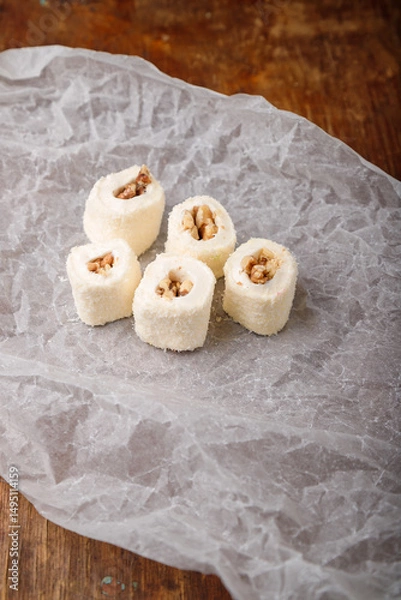 Obraz Turkish delight, white locum roll with walnut and coconut flakes on white paper, wooden background. Eastern sweets, oriental food. Traditional dessert