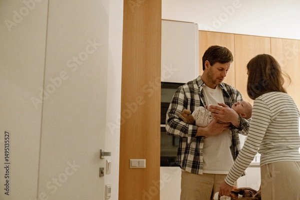 Fototapeta A mother stands and looks at her child, who is being held in the arms of a father, who is standing opposite her