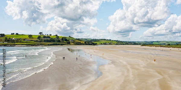Fototapeta The idyllic beach scene reveals people relaxing and enjoying the weather. The serene atmosphere is enhanced by the rolling hills in the distance.