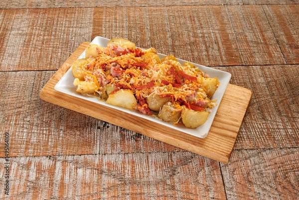 Obraz A plate of food with potatoes and cheese on top. The plate is on a wooden board