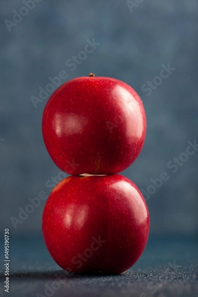 Fototapeta Two shiny red apples balanced vertically against a blue background.