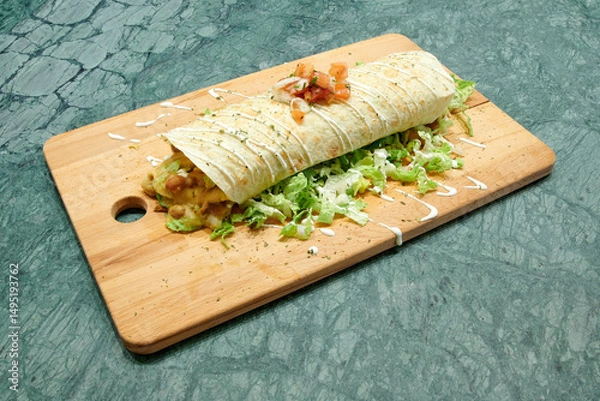 Obraz A burrito with lettuce and cheese on top of a wooden cutting board. The burrito is wrapped in a tortilla