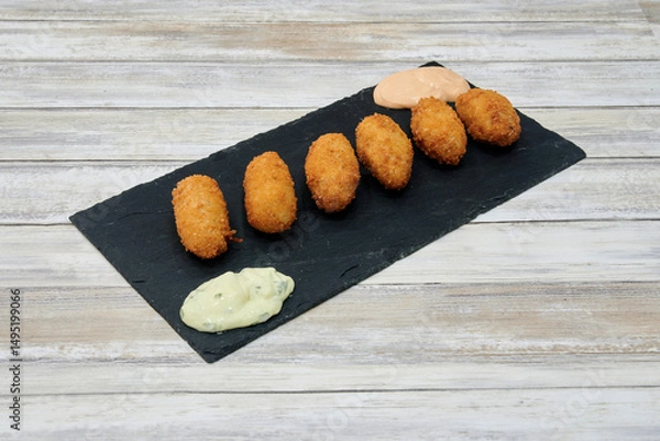 Obraz A plate of fried food with a dipping sauce. The food is small and round. There are six pieces of food on the plate