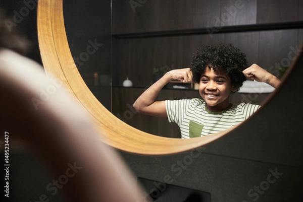 Fototapeta African American boy smiling while flexing his muscles in bathroom mirror, Being proud and confident with curly hair and round mirror