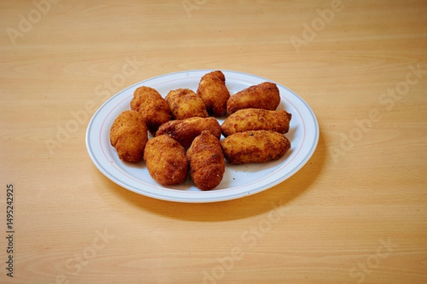 Obraz A plate of fried chicken pieces sits on a wooden table. The chicken pieces are golden brown and appear to be seasoned well