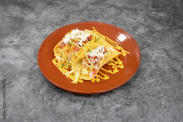 Fototapeta A plate of two tacos with cheese and lettuce on top. The plate is on a grey counter