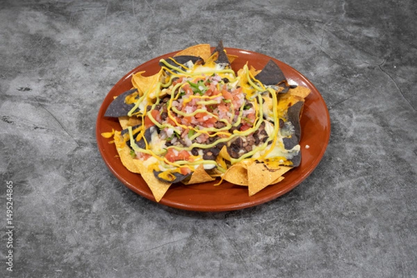 Fototapeta A plate of nachos with cheese and sour cream. The nachos are topped with tomatoes, onions, and green sauce