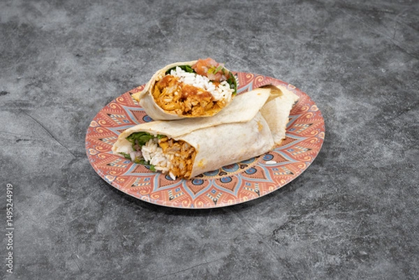 Fototapeta A burrito is on a plate. The plate is red and white. The burrito is wrapped in a tortilla