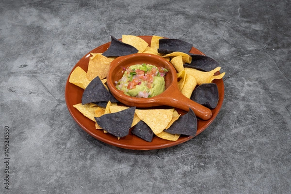 Fototapeta A plate of tortilla chips with a bowl of guacamole. The bowl is in the center of the plate and the chips are scattered around it