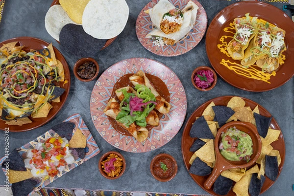 Fototapeta A table with many different types of food, including tacos, enchiladas, and nachos