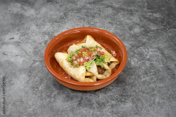 Fototapeta A bowl of food with three tortillas in it. The tortillas are covered in salsa and topped with lettuce