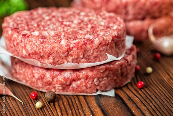 Fototapeta paszteciki hamburger surowego mięsa wołowego na papierze, suchą papryką i czosnkiem na podłoże drewniane