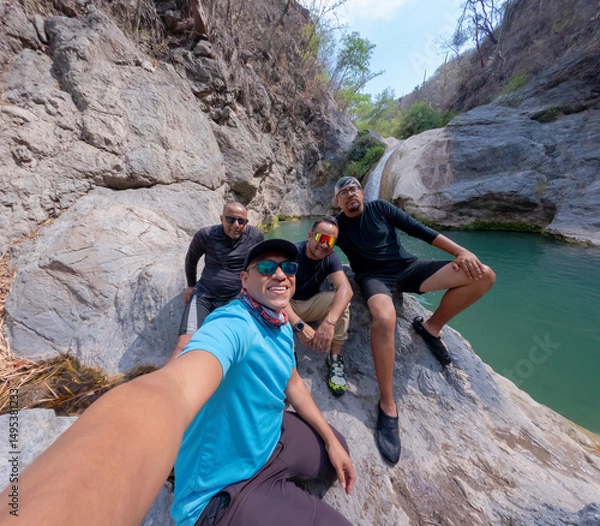 Obraz Four male hikers taking a selfie near a waterfall in a rocky canyon