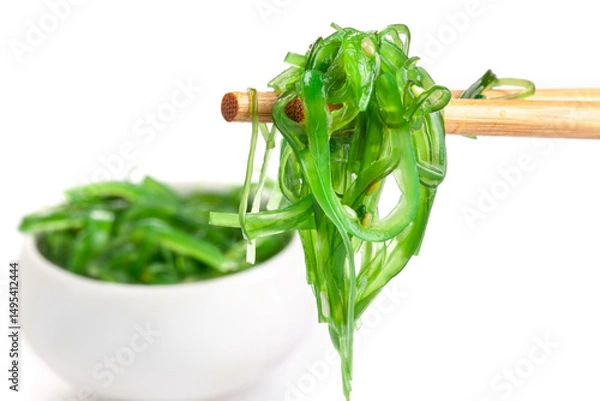 Fototapeta Chopsticks holding Japanese seaweed salad. Japanese cuisine - Wakame salad, Chuka seaweed salad isolated on a white background.