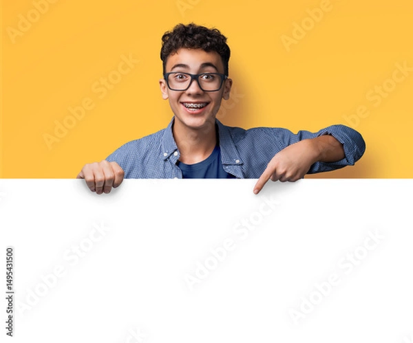 Fototapeta Portrait image -  happy man wear glasses, braces stand behind blank empty banner mockup sign board signboard, advertise show, point finger free space for ad text isolate yellow background. Dental care