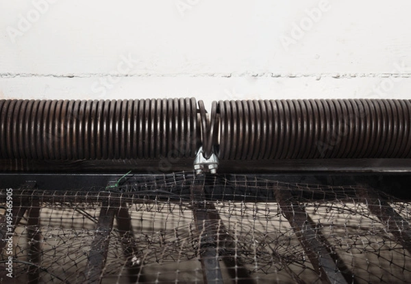 Fototapeta Clamped garage door spring or torsion spring on overhead sectional door. Close up of temporary quick clamp or emergency repair after spring sheared-off on parking gate on ceiling. Selective focus.