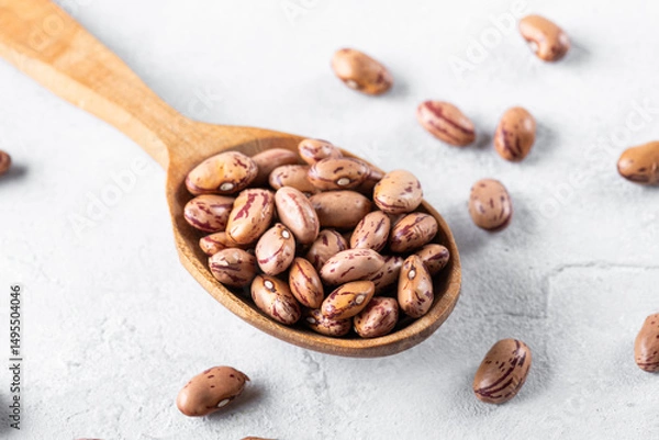 Obraz Borlotti beans on a wooden spoon on a gray table surface. Popular in Mediterranean diets, these legumes are rich in fiber and protein, often used in soups and stews