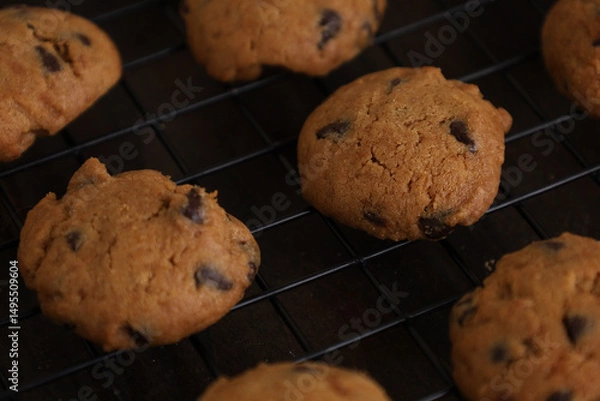 Obraz Chocolate chip cookies lined up on a black cooling rack on a wooden table, copy space. Flat top view photo.
