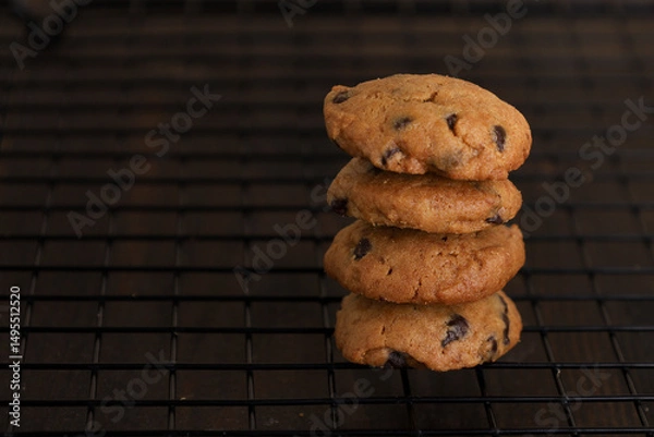 Obraz chocolate chip cookies stacked on black cooling wire rack on dark wooden table