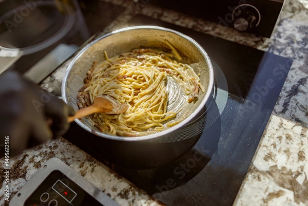 Obraz A skilled chef energetically stirs freshly cooked spaghetti in a beautifully stylish and modern kitchen setting
