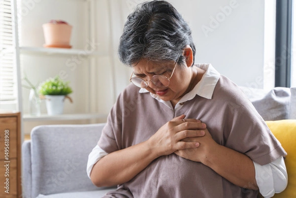 Fototapeta Asian elderly grabbing her chest and feeling pain from heart attack suddenly at home.