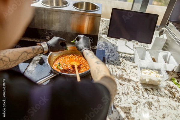 Obraz In a modern culinary setting, a talented chef is skillfully preparing a vibrant and rich red sauce with flair