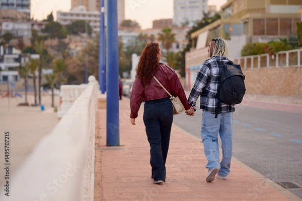 Fototapeta Couples enjoy a romantic stroll along the beach at sunset in a coastal town