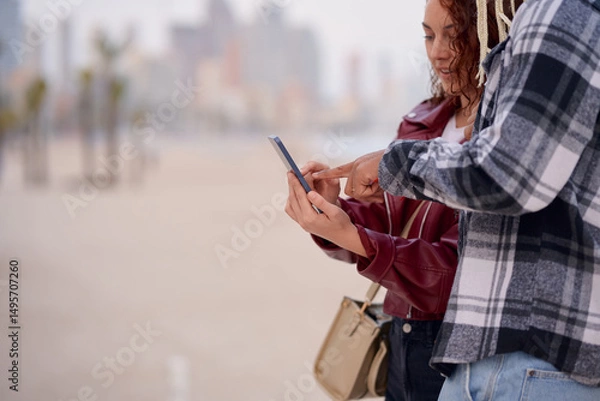Fototapeta Couple exploring a mobile application on a beach with city skyline in background
