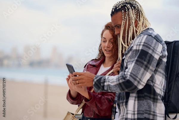 Fototapeta Friends sharing exciting moments on a beach with a smartphone