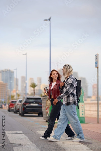Fototapeta Two friends walking along a city street with coffee in hand on a sunny day