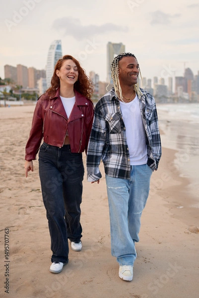 Fototapeta Couple walks hand in hand on the beach during sunset in a cityscape