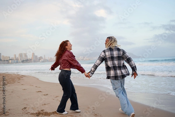 Fototapeta Couple enjoys a romantic beach walk during sunset near the city