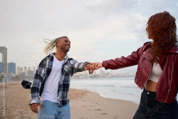 Fototapeta Joyful couple enjoying a beach walk during sunset near the city