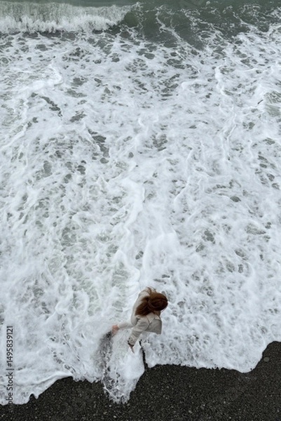 Fototapeta Girl walking along the seashore in stormy waves. Top view