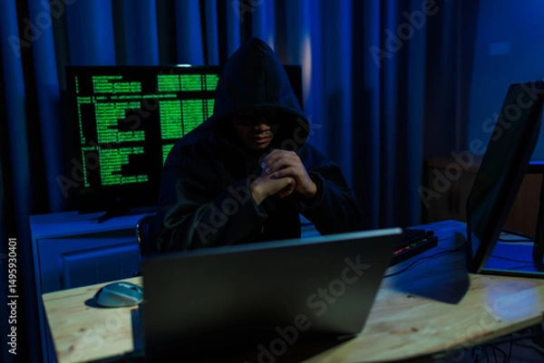 Fototapeta Male hacker in a dark room trying to steal global user data to sell on the dark web, representing serious threats in modern cybercrime.