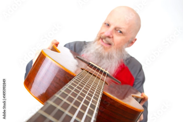Obraz Senior bald man with a thick gray beard poses with an acoustic guitar, dressed in a gray sports shirt, isolated on a white backdrop, highlighting a passionate musical expression.
