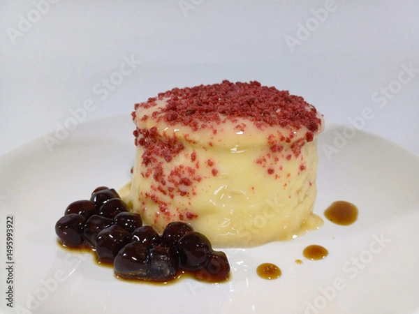 Fototapeta A single, delicate souffle pancake, characterized by its light and airy texture, is presented on a white plate. The pale yellow pancake is topped with a sprinkling of vibrant red crumbs and a drizzle