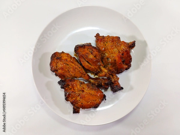 Fototapeta Four pieces of succulent grilled sweet spicy chicken wings are neatly arranged on a clean white plate. The wings boast a glossy, reddish-brown glaze with subtle charring, indicating a delicious finish