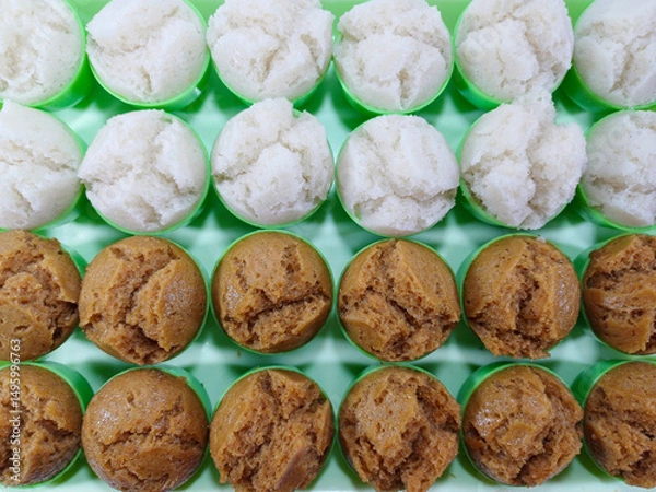 Fototapeta Rows of Kue Apem, small, fluffy steamed rice flour cakes, are meticulously arranged on a bright green silicone mat. The delicate Indonesian desserts come in two variations: pristine white and rich