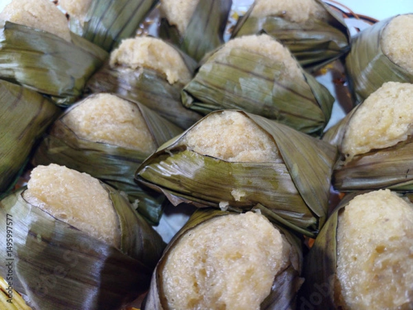 Fototapeta A pyramid-shaped Beppa Oto, a Bugis delicacy often made as a banana cake, is meticulously wrapped in fresh green banana leaves, resting on a surface. This traditional steamed cake offers a sweet treat