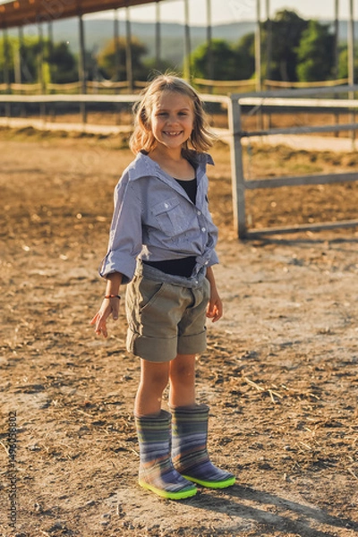 Obraz Vertical portrait of farmer kid girl spend time on a farm in summer. Happy childhood in the countryside. Happy summertime.